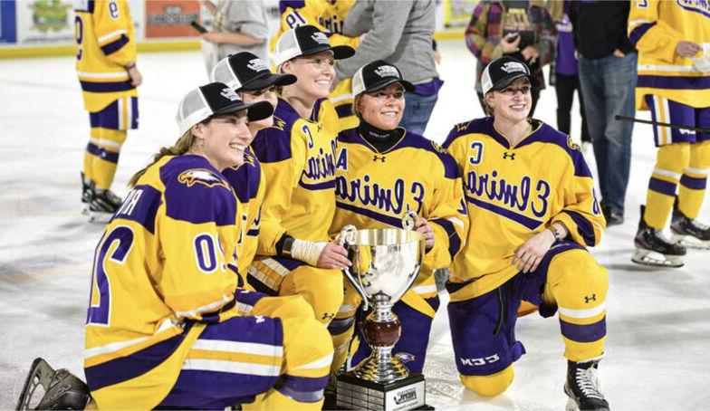 Members of the women's hockey team wear championship hats as they pose on the ice with a trophy