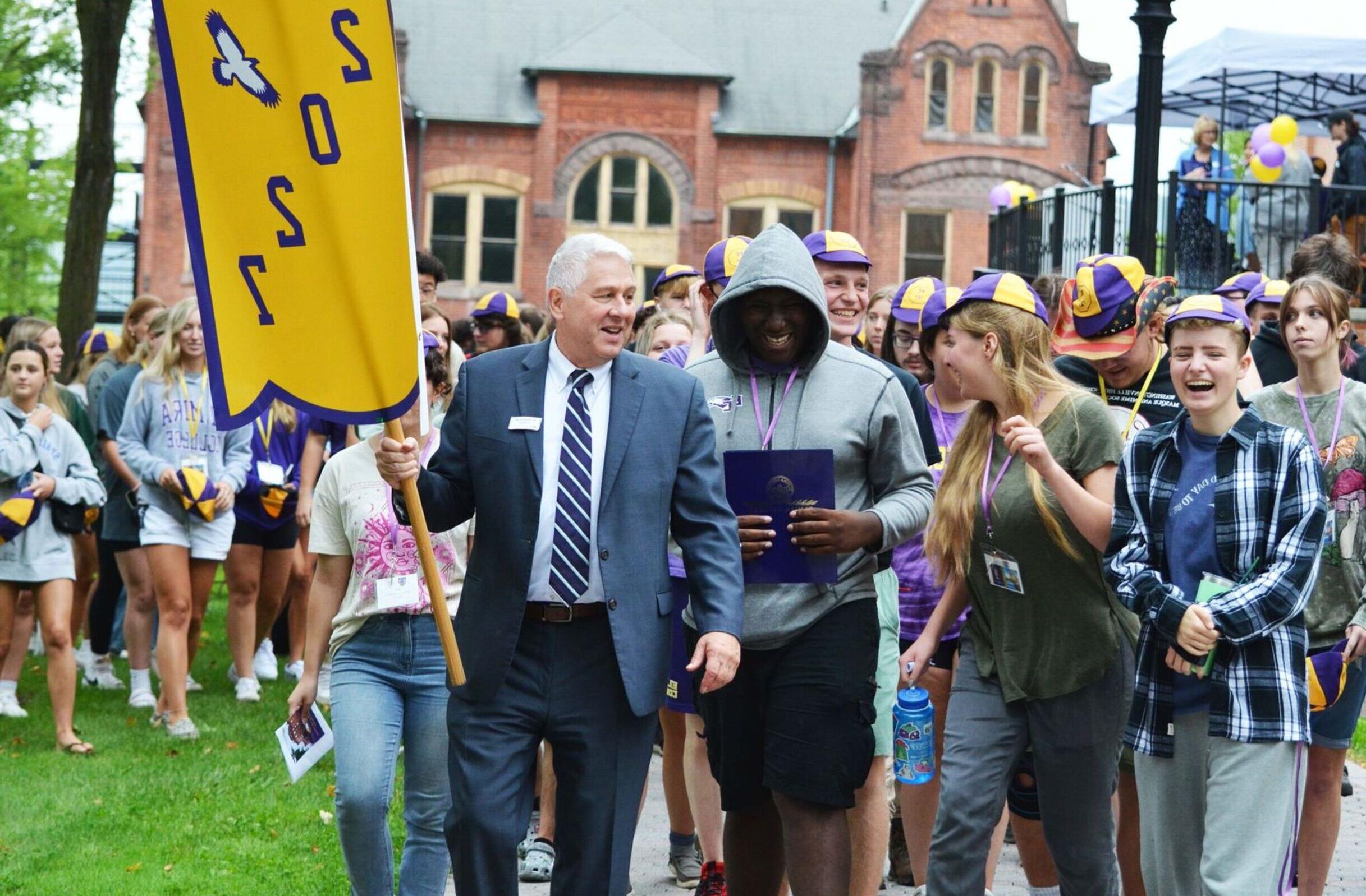 President Charles Lindsay holds a 2027 flag as he leads a procession of new students following the fall welcome.